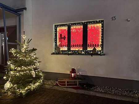 Das vom ATZ gestaltete Adventsfenster zum 4 Dezember, mit einem Weihnachtsbaum davor.